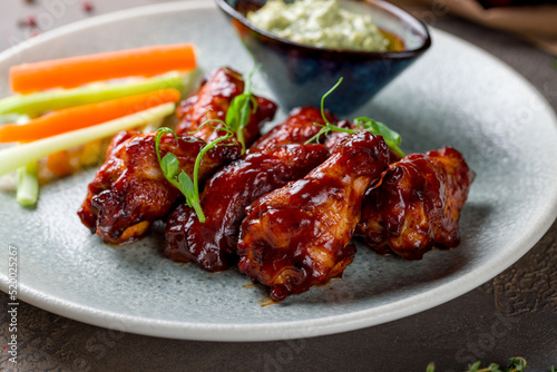 chicken wings in barbecue sauce on plate with blue cheese sauce macro close up on brown stone table