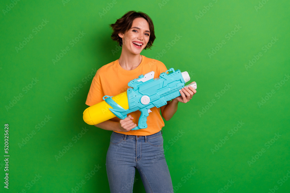 Portrait of positive charming girl toothy smile hands hold water pistol isolated on green color background Portrait of positive charming girl toothy smile hands hold water pistol isolated on green color background