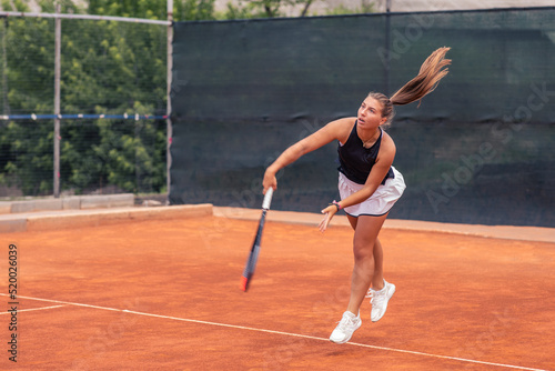 In a luminous summer day on the professional tennis court good looking woman playing the tennis she hitting the ball very hard with the racket