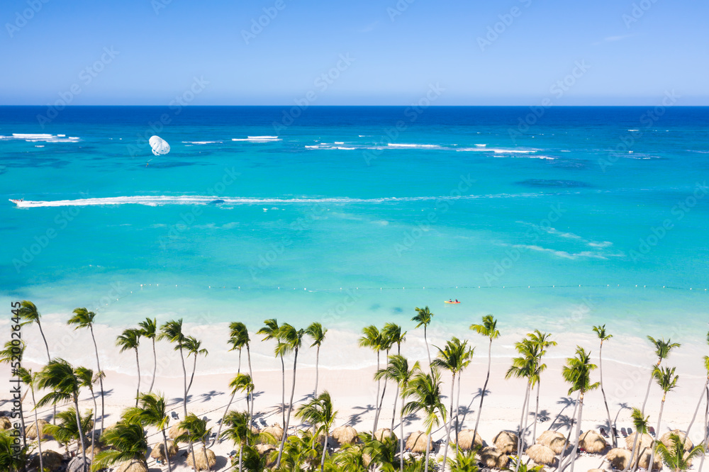 Bounty and pristine shore with resorts, palm trees, caribbean sea and people relaxing on beach. Tropical vacation. Dominican Republic. Aerial view