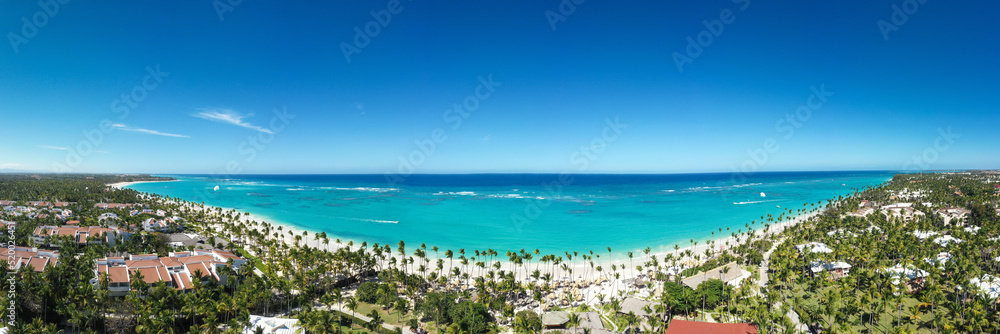 Bounty and pristine shore with resorts, palm trees, caribbean sea and people relaxing on beach. Tropical vacation. Dominican Republic. Aerial panoramic view