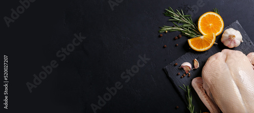Raw and uncooked whole duck on slate board on black background