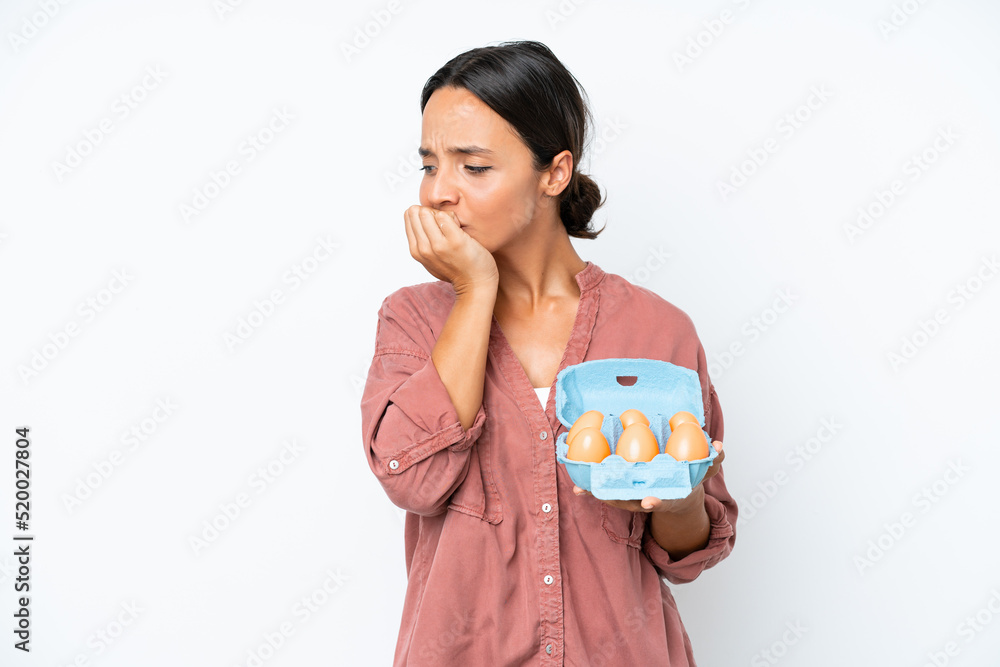 Young hispanic woman holding eggs isolated on white background having doubts Young hispanic woman holding eggs isolated on white background having doubts