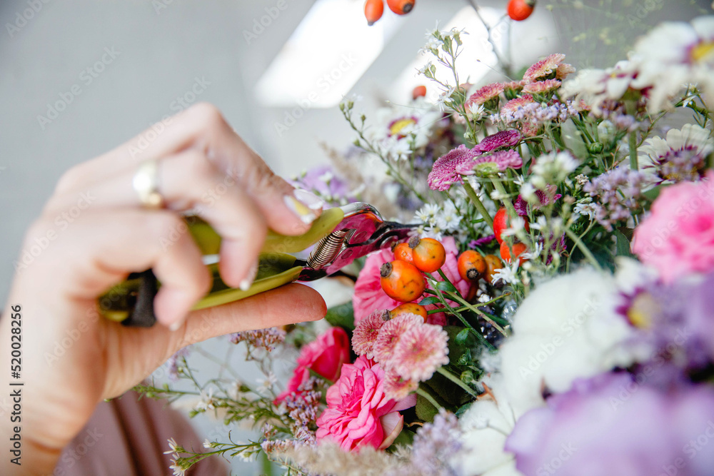 the florist with the help of a secateurs cuts the elements of the bouquet from fresh multi-colored flowers. Close-up