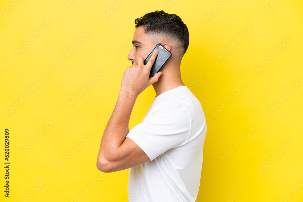 Young Arab handsome man isolated on yellow background keeping a conversation with the mobile phone with someone Young Arab handsome man isolated on yellow background keeping a conversation with the mobile phone with someone