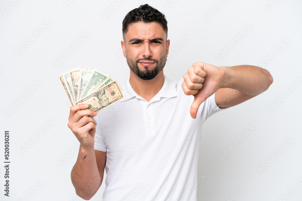 Young Arab man taking a lot of money isolated on white background showing thumb down with negative expression Young Arab man taking a lot of money isolated on white background showing thumb down with negative expression
