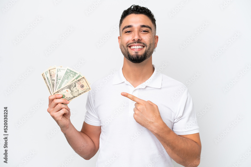 Young Arab man taking a lot of money isolated on white background pointing to the side to present a product Young Arab man taking a lot of money isolated on white background pointing to the side to present a product