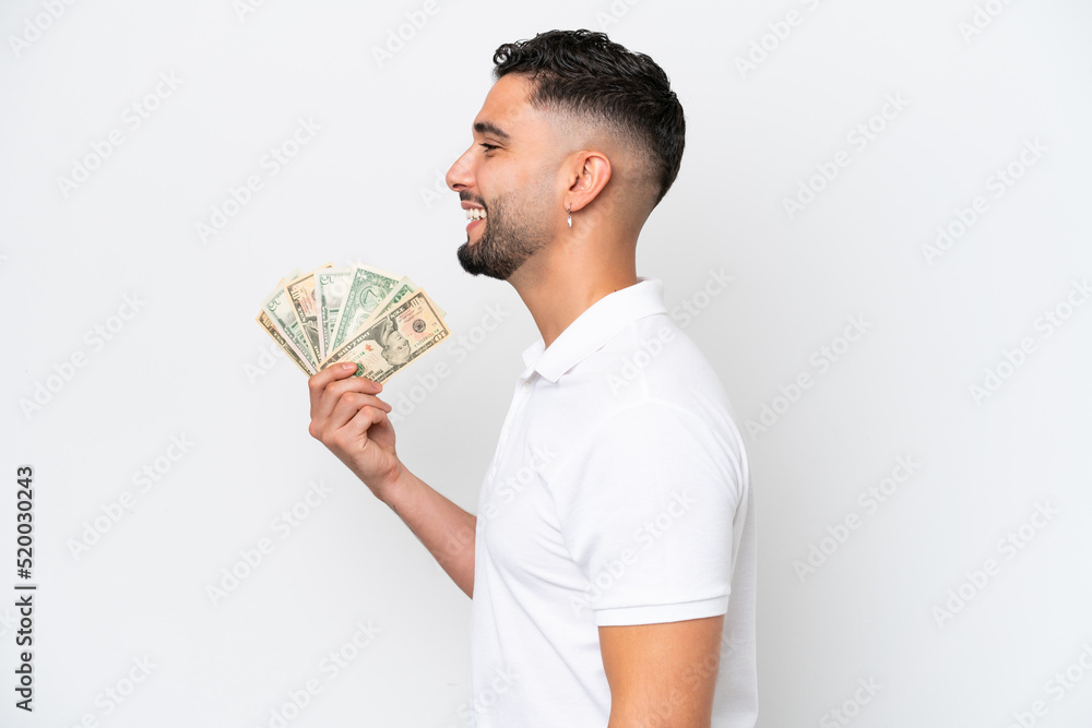 Young Arab man taking a lot of money isolated on white background laughing in lateral position Young Arab man taking a lot of money isolated on white background laughing in lateral position