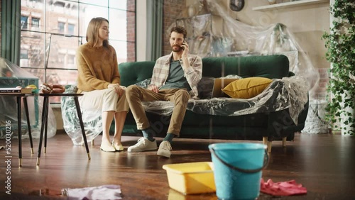 Roof is Leaking or Pipe Rupture at Home: Panicing Couple Calling Insurance Company, have Positive Answer and Celebrate with Hug that the Nightmare is Ending. Water Drips into Buckets in Living Room photo