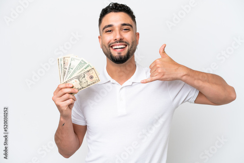 Young Arab man taking a lot of money isolated on white background making phone gesture. Call me back sign © luismolinero