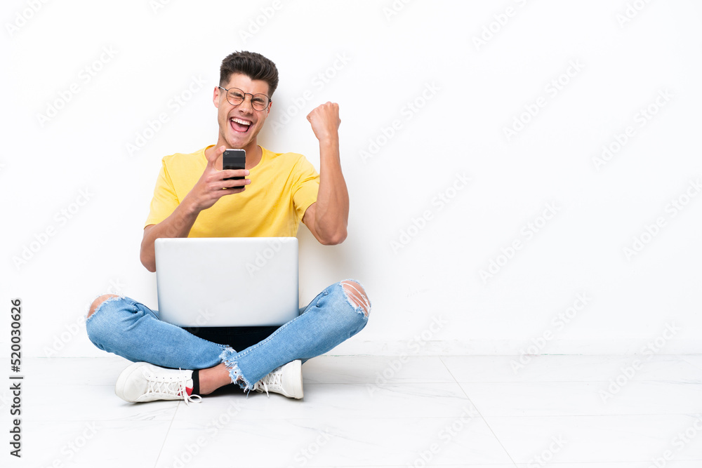 Young man sitting on the floor isolated on white background with phone in victory position Young man sitting on the floor isolated on white background with phone in victory position