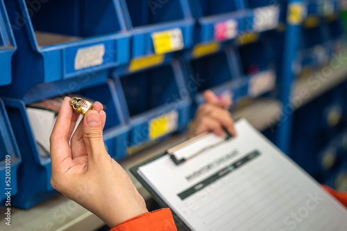 A worker's hand is holding metal ring object, a machinery spare part  with blurred background of storage shelf. Industrial working scene photo, selective focus.