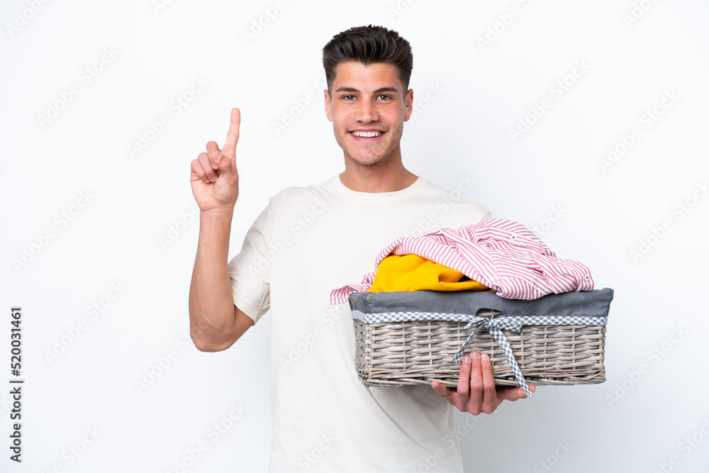 Young caucasian man holding laundry basket isolated on white background pointing up a great idea Young caucasian man holding laundry basket isolated on white background pointing up a great idea