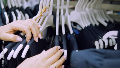 Close-up of a woman sorting through hangers with a school uniform in a clothing store.