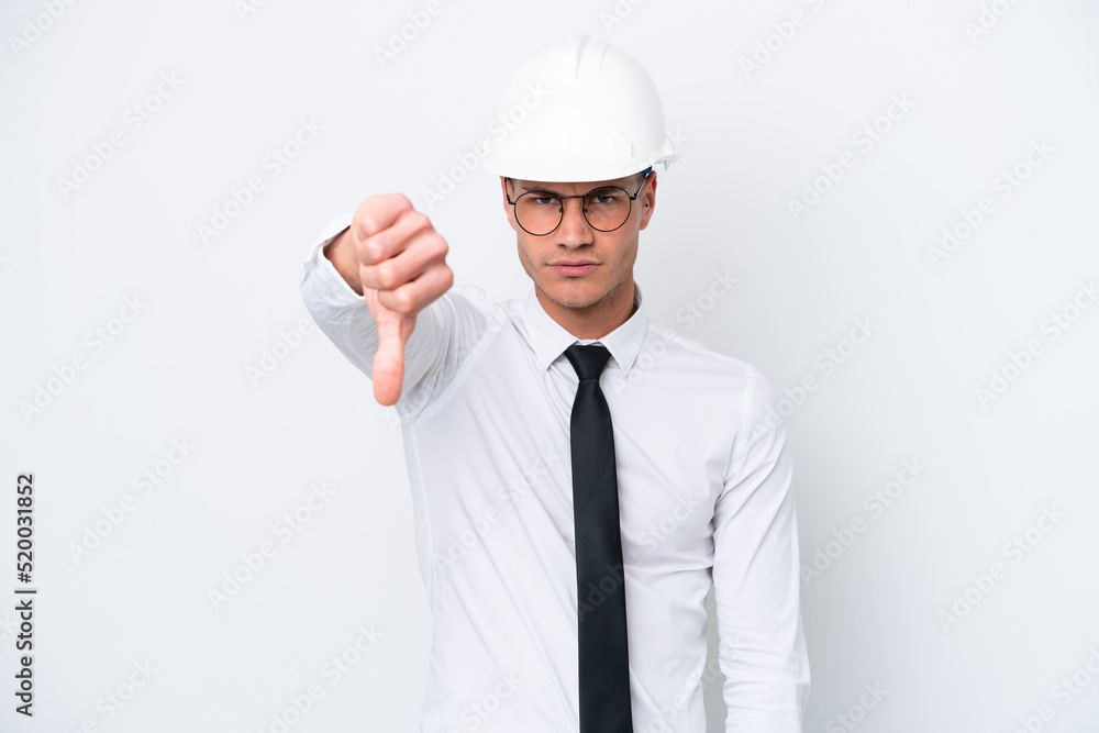 Young architect caucasian man with helmet and holding blueprints isolated on white background showing thumb down with negative expression Young architect caucasian man with helmet and holding blueprints isolated on white background showing thumb down with negative expression