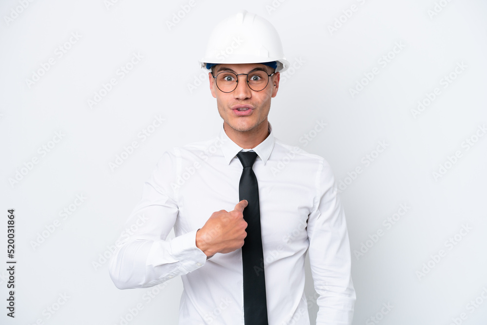 Young architect caucasian man with helmet and holding blueprints isolated on white background with surprise facial expression