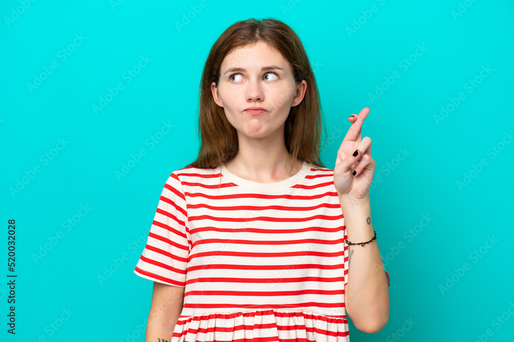 Young English woman isolated on blue background with fingers crossing and wishing the best Young English woman isolated on blue background with fingers crossing and wishing the best