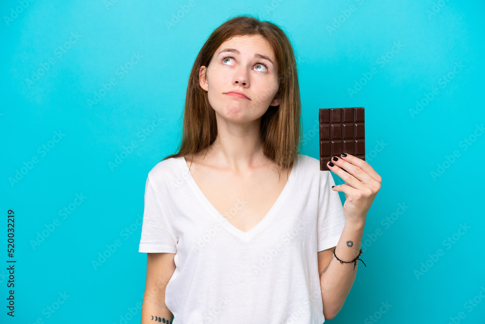 Young English woman with chocolat isolated on blue background and looking up Young English woman with chocolat isolated on blue background and looking up