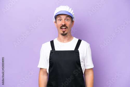 Fishmonger man wearing an apron isolated on purple background with surprise facial expression