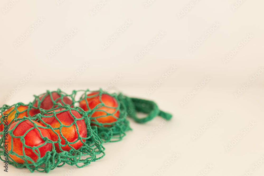 summer background , peaches in a green eco bag on a white background . Place for text, selective focus, horizontal format
