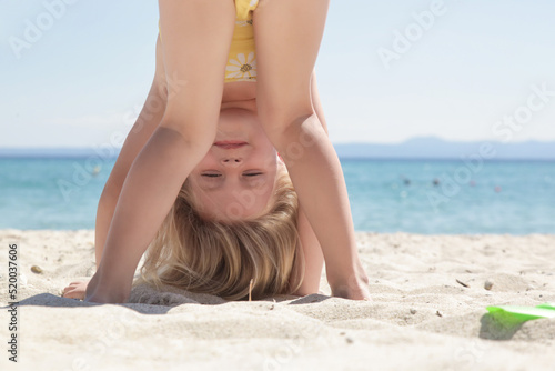 Foto Happy little girl standing upside down on the sandy beach