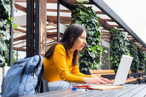 Young Latina student woman with indigenous features using her laptop at a table outside