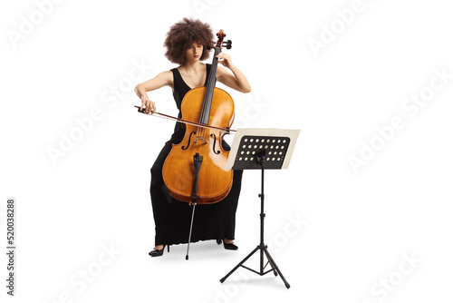 Young woman in a black dress playing cello and reading from a music paper on a stand