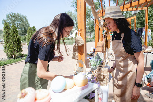 Foto Young brunette girl buyer with long hair and woman seller in apron and hat on ei