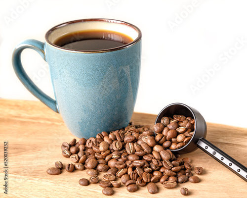 Coffee beans spilling from a scoop with a green mug of coffee