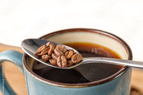 Coffee beans in a spoon balanced over a green mug of coffee