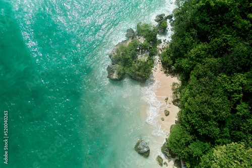 aerial drone view of padang padang beach in bali with waves, rocks and forest © JX