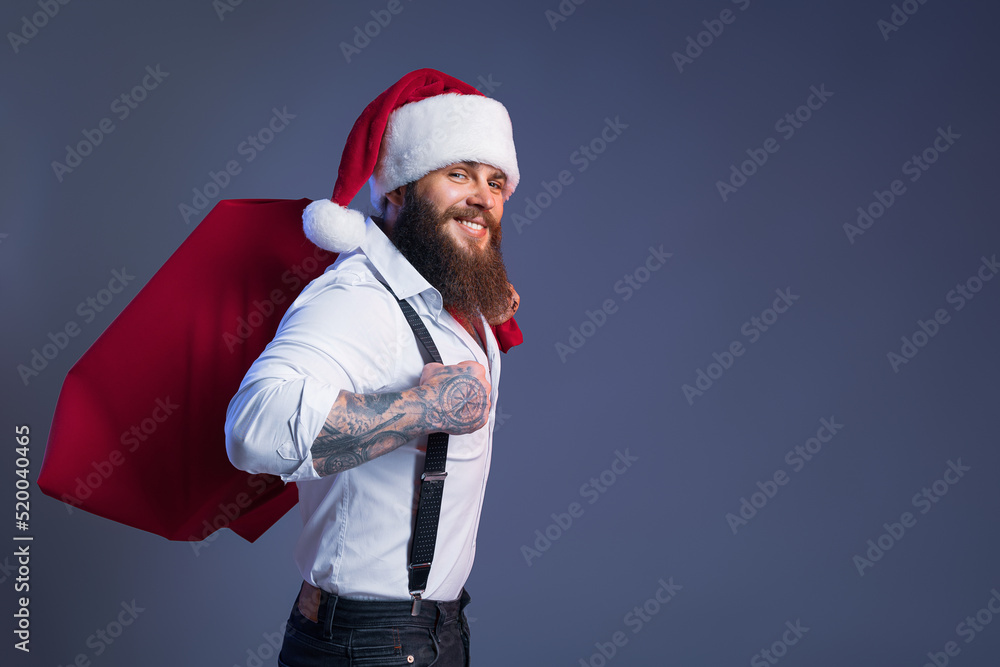 Smiling bearded man in Santa's hat carries big sack with presents. Christmas sales. New Year concept