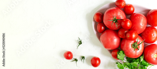 Red ripe tomatoes of different sizes with a sprig of parsley on a pink large plate on a white background. Healthy food concept. Horizontal orientation. Selective focus. copy space. Top view. Banner