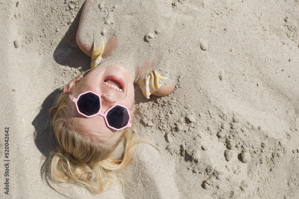 Cute happy little girl buried in the sand on the beach. Stock Photo