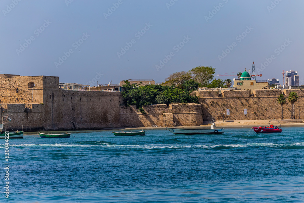 Acre Acco, Israel, June 2022 : view from the sea to the bay, pier, fortress wall and fishing boats in the old city of Acre or Acco in northern Israel at the Mediterranean Sea.