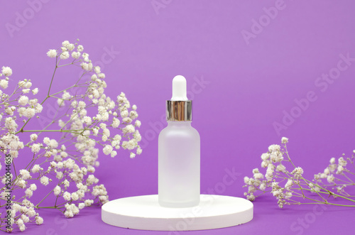 Cosmetic bottle with a dropper on a white podium with a bouquet of gypsophila. Skin care cosmetics