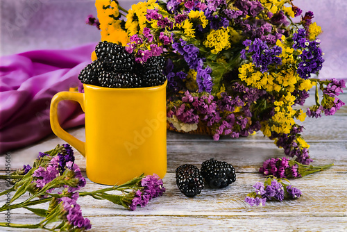 Fresh blackberry berries in a cup. Yellow cup and dry statice flowers. Bright summer composition.