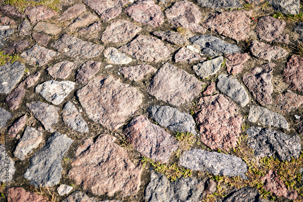 Closeup detail of road paved with block stone and overgrown by grass. 