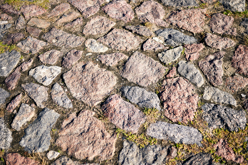 Closeup detail of road paved with block stone and overgrown by grass. 