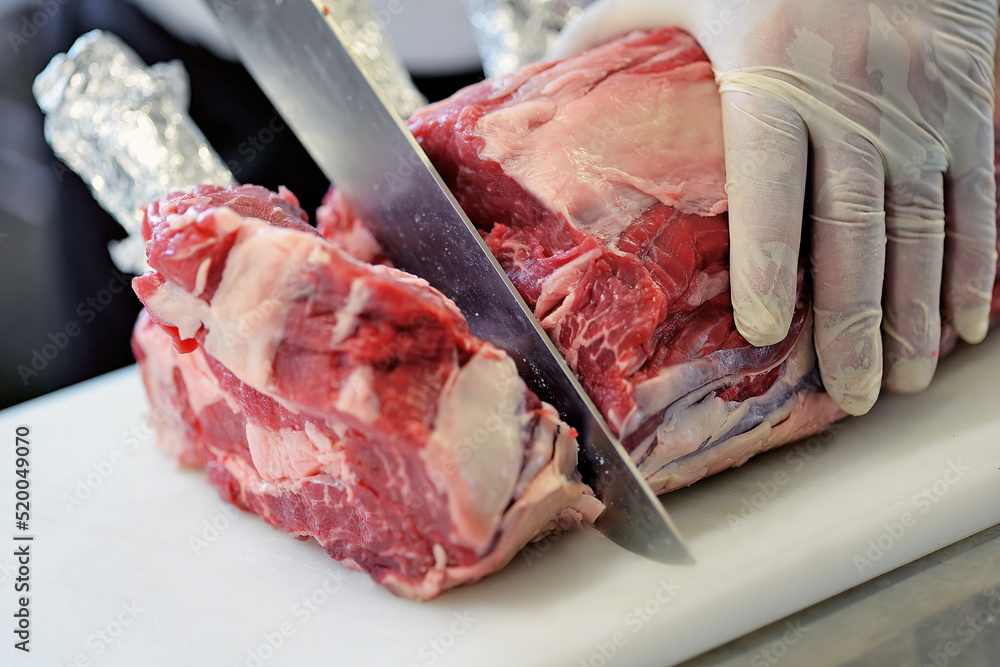 Butcher cuts rack of ribeye steak on white cutting board