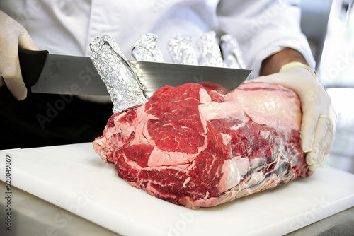 Butcher cuts rack of ribeye steak on white cutting board