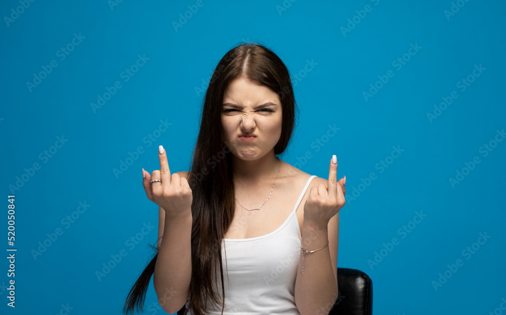 Portrait of rude vulgar woman showing middle fingers, impolite gesture of disrespect, looking with aggression hate on blue background. Portrait of rude vulgar woman showing middle fingers, impolite gesture of disrespect, looking with aggression hate on blue background.