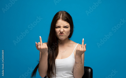 Bilde på lerret Portrait of rude vulgar woman showing middle fingers, impolite gesture of disrespect, looking with aggression hate on blue background