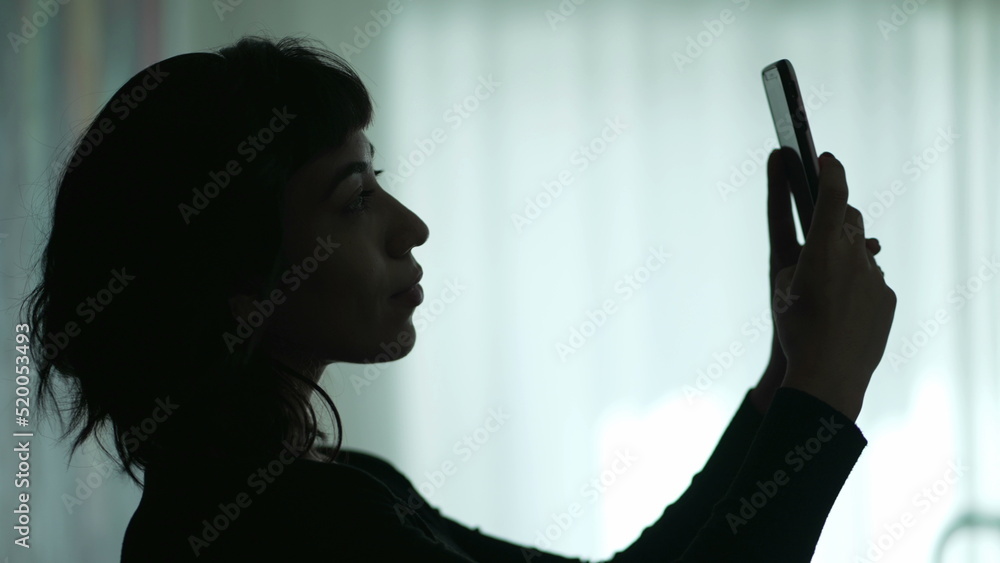 Girl taking selfie with phone. Silhouette of one young woman holding smartphone takes photo with cellphone camera Girl taking selfie with phone. Silhouette of one young woman holding smartphone takes photo with cellphone camera