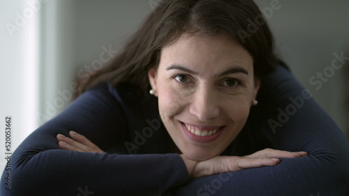 Portrait of woman in her 30s smiling at camera leaning on table with arms crossed closeup face