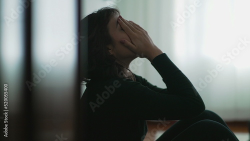 Depressed woman sitting on floor covering face with hands in despair photo