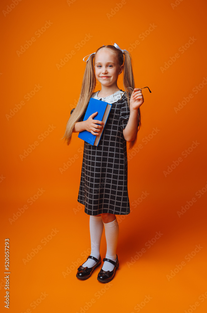 Back to school. A schoolgirl holds a blue book against an isolated yellow studio background. Back to school. A schoolgirl holds a blue book against an isolated yellow studio background.