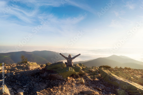 Girl with raised arms on mountain top looking at beautiful mountain valley in fog at sunset. Beautiful morning landscape in mountains. Travel and tourism. © Артур Ничипоренко