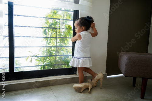 Niña feliz y traviesa con los zapatos tacones de su mamá jugando a ser grande, divertida posando y haciendo travesuras photo