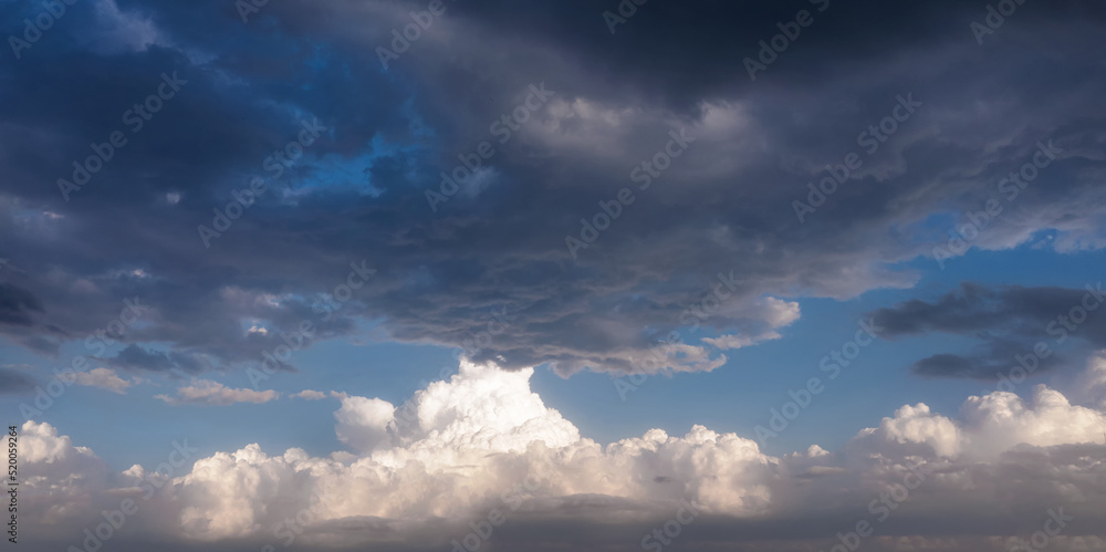 Dramatic sky with dark stormy clouds and white cumulus clouds near horizon